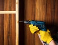 Woodworker drills a hole with an electric drill in a wood board. Close up of foreman hand at work. Working environment in