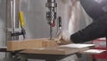 Woodworker drills holes in wooden plank with drilling machine in slow motion.