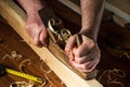 Woodworker using a hand plane to clean up a wooden board. Hands of the master closeup at work. Working environment in a carpentry