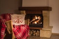 Wool warm blanket or plaid and a pillow on the rattan armchair on the background of burning fireplace