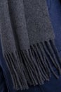 Woolen grey scarf with fringe on blue pullover. Closeup view.