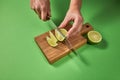 Slices of natural organic green lime, cutting by female hands on a wooden board on green background with copy space. Royalty Free Stock Photo