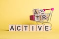 The word ACTIVE on wooden cubes, on a yellow background with a shopping trolley