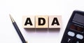 The word ADA is written on wooden cubes between a pen and a calculator on a light background Royalty Free Stock Photo