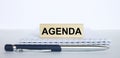 The word Agenda on a bar of jenga wood, lying on a Notepad with a metal blue pen Royalty Free Stock Photo