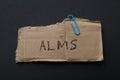 The word `alms` on a piece of cardboard on a black background.