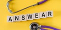 Word ANSWEAR building from wooden cubes on yellow desk with stethoscope