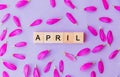 Word april made up of wooden blocks and flower petals on purple background