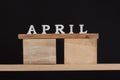 Word April written on wooden blocks on wooden shelf on black background. Spring calendar