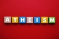 Word Atheism made of wooden cubes with letters on red table, top view