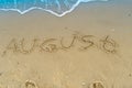 The word August is written on the sand of a beach by the sea. Washed off by a wave. The inscription disappears. End of Royalty Free Stock Photo