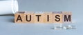 Word AUTISM. Autism text on wooden blocks. In front of a row of cubes are ampoules, in the background - white plastic packaging