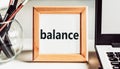 The word balance in a wooden frame on a table with a laptop and pens. Business concept Royalty Free Stock Photo