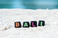 Word Bali is made of multicolored letters on snow-white sand against the blue sea.