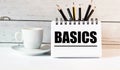 The word BASICS is written in a white notepad near a white cup of coffee on a light background Royalty Free Stock Photo