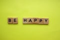 The word Be Happy is made of wooden cubes on a yellow background. Happiness, motto, birthday, optimism.