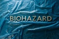 The word biohazard laid with silver letters on blue crumpled plastic film background in flat lay composition at center Royalty Free Stock Photo