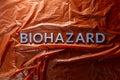 The word biohazard laid with silver letters on red crumpled plastic film background in flat lay composition at center Royalty Free Stock Photo