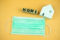 Word block `HOME` and wooden white home with green medical face mask to prevent from covid19 Royalty Free Stock Photo