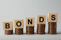 Word Bonds made of wooden cubes with letters on stacked coins against light grey background