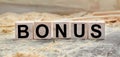 The word BONUS is written on wooden cubes. Wooden cubes lie on the table with sawdust and wooden blocks. Designed to promote your