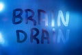 The words brain drain written on night wet window glass close-up with blurred background in classic blue color