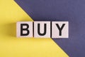 Word BUY on wooden cubes on yellow - gray background