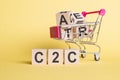 The word C2C - Consumer to consumer, on wooden cubes, on a yellow background with a shopping trolley Royalty Free Stock Photo