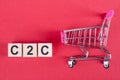 The word C2C - consumer-to-consumer, on wooden cubes, on a pink background with a shopping trolley Royalty Free Stock Photo