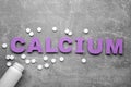 Word Calcium made of violet paper letters, medical bottle and pills on gray background, top view Royalty Free Stock Photo