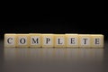 The word COMPLETE written on wooden cubes isolated on a black background