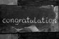 The word congratulation written with chalk on black stone.