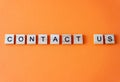 Word contact us. The phrase is laid out in wooden letters top view. Orange flat lay background.