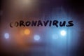 The word coronavirus handwritten on night foggy glass in teal-orange colors
