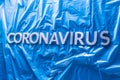 Word coronavirus laid with silver letters on crumpled blue plastic coat - in perstpective view with selective focus Royalty Free Stock Photo