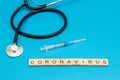 Word CORONAVIRUS made from wooden cubes on blue with Stethoscope and surgical syringe
