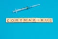 Word CORONAVIRUS made from wooden cubes and and surgical syringe on blue background