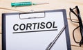 The word CORTISOL is written on a white piece of paper next to black-rimmed glasses, a pen and a syringe. Medical concept Royalty Free Stock Photo