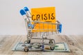 The word `crisis` on a sticker in a shopping cart. dollars on a wooden background. Side view.