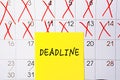 The word Deadline writing on a yellow sticky note posted on a calendar or planner page as a reminder. Closeup of a personal agenda