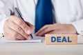 The word deal written on a wooden block with a businessman signing a paper at the background Royalty Free Stock Photo