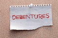 The word debentures in Brazilian Portuguese written on a piece of paper on a wooden table.