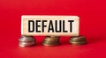 The word DEFAULT is written on a wooden block that stands on coins and a red background.