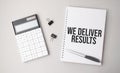 The word We Deliver Results is written on a white background next to a pen ,calculator and reports. Business concept Royalty Free Stock Photo