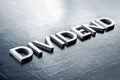 The word dividend laid by volumetric silver metal letters on gloss painted board background with selective focus