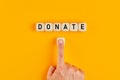 The word donate written on wooden cubes with a male hand pushing the button for donation. Charity concept