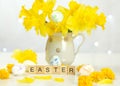 Word Easter on wooden cubes. Easter composition of a bouquet of daffodils and multi-colored eggs