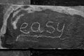 The word EASY written with chalk on black stone. Royalty Free Stock Photo