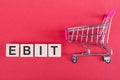 The word EBIT, on wooden cubes, on a pink background with a shopping trolley