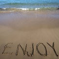 Word enjoy written on sand